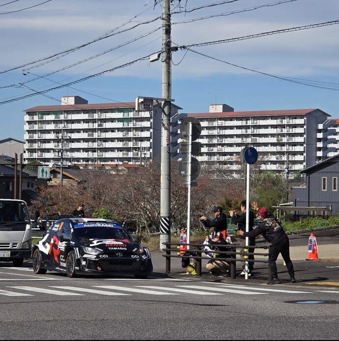 街中を走るラリーカーと撮影する観客