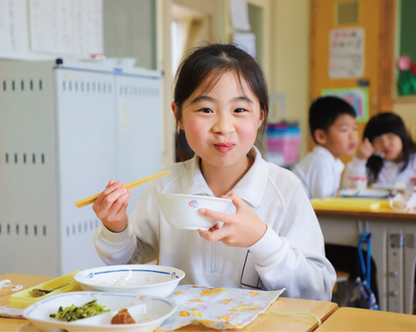 市内小学校で給食を食べて笑顔の女の子