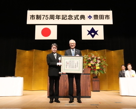 壇上で記念撮影をする市政功労者の三宅英臣氏と太田市長